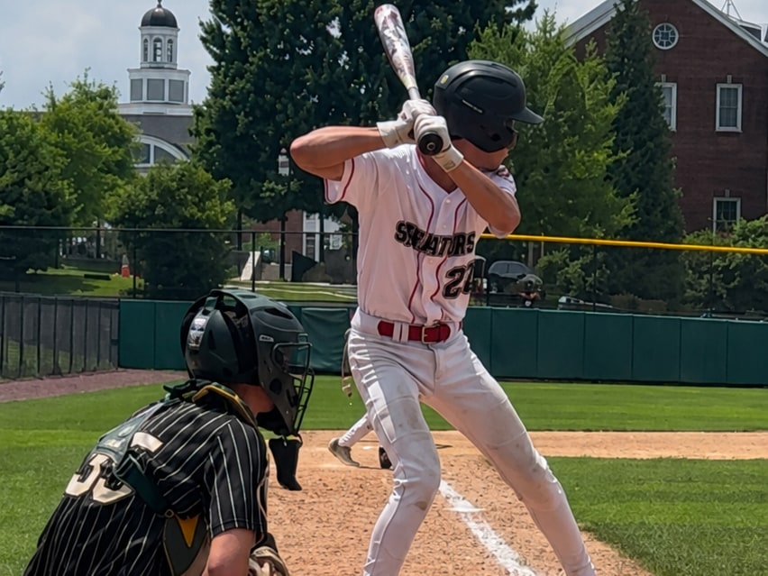 Alex Vasquez at the plate in a white Senators uniform, bat cocked in his stance with the catcher set behind him